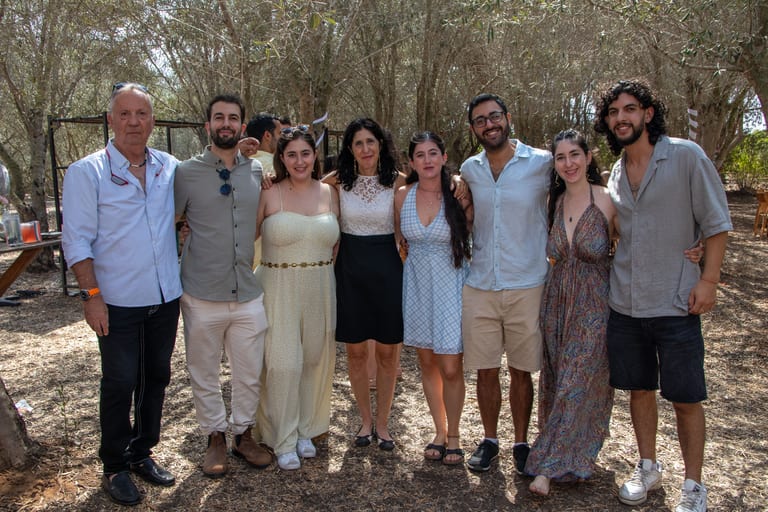 שמונה אורחים עומדים בשורה ומצטלמים מתחת לעצים