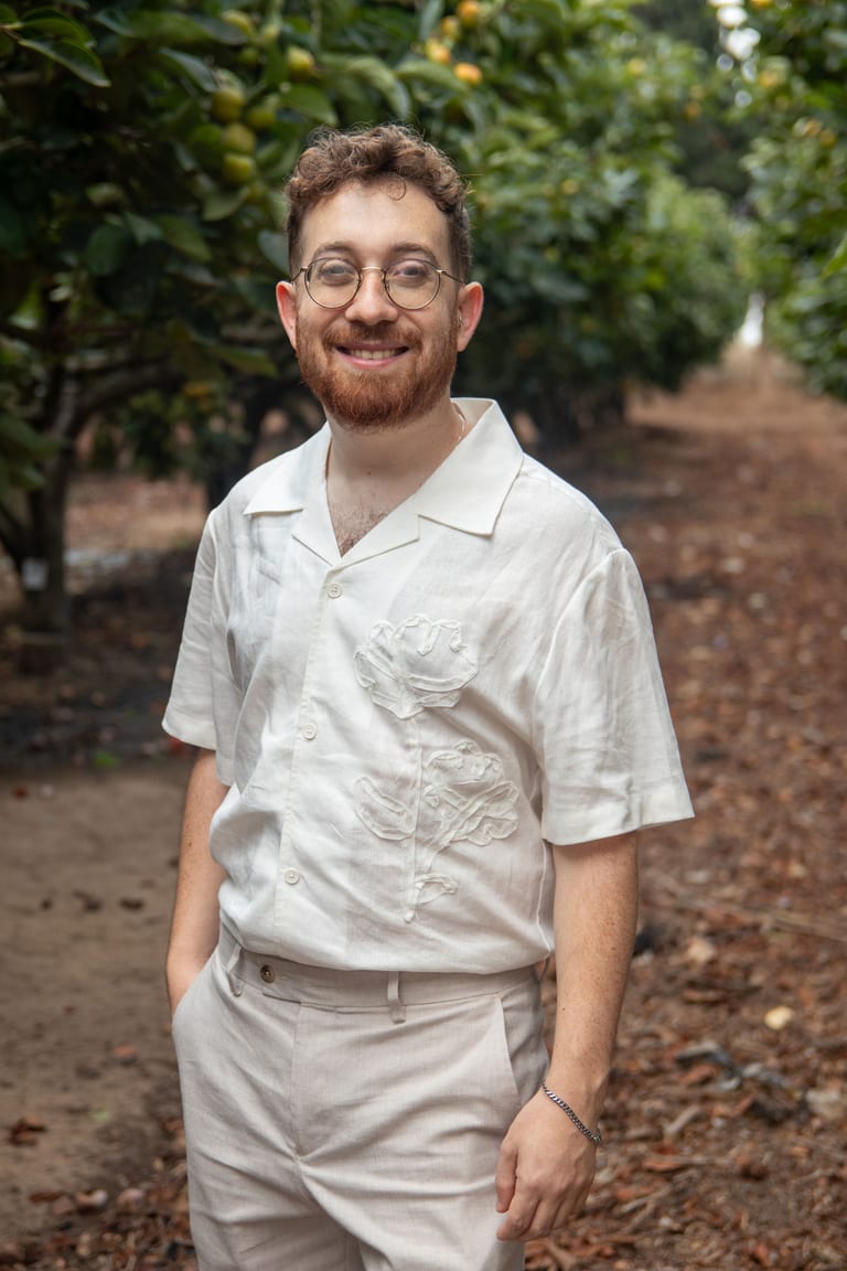 החתן עומד מחייך בפרדס, ידיים בכיסים