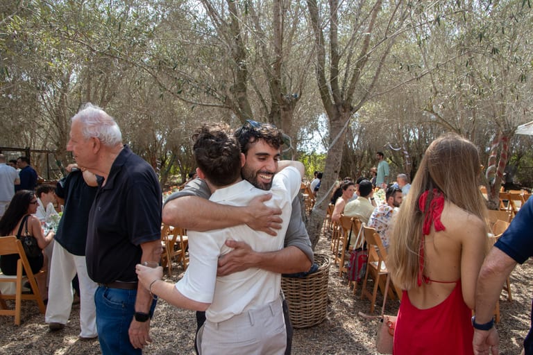 גבר מחבק גבר מבוגר בחורשת זיתים, אורחים סביבם